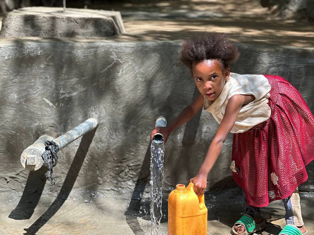 Young girl at a Hawassa Hope clean water project site with a jug letting water flow into it. 