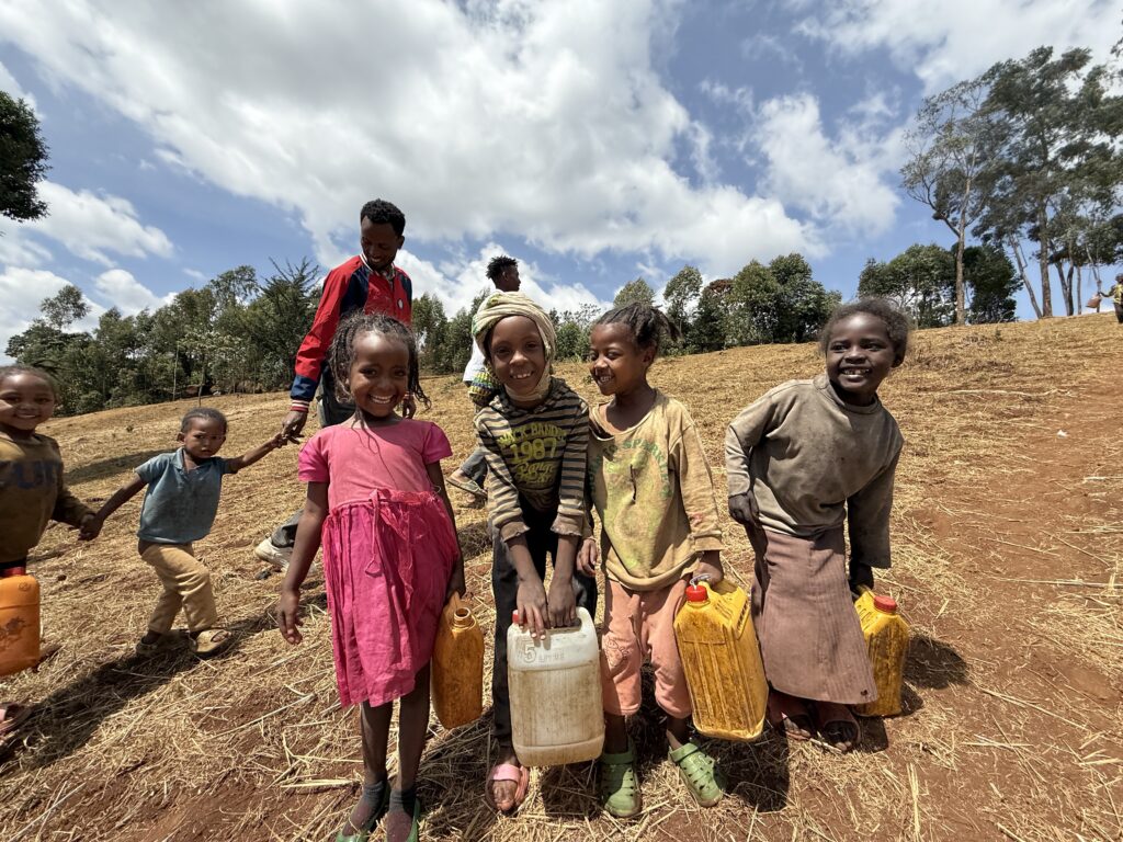 4 young girls in Ethiopia with water jugs walking back up a dry barren hill. They paused for picture and have big smiles on their faces. They have just left Hawassa Hope's clean water site. 