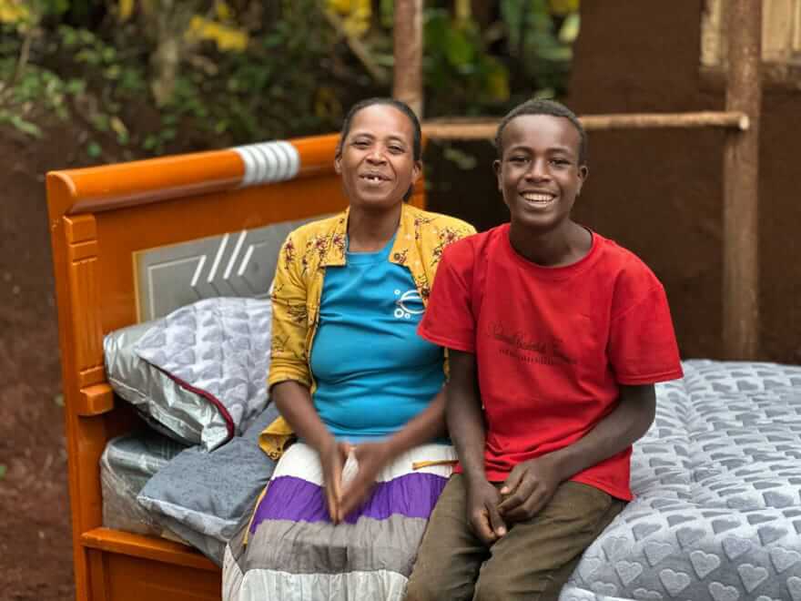 A mom and son sits on a bed outside their newly built home by Hawassa Hope in Ethiopia